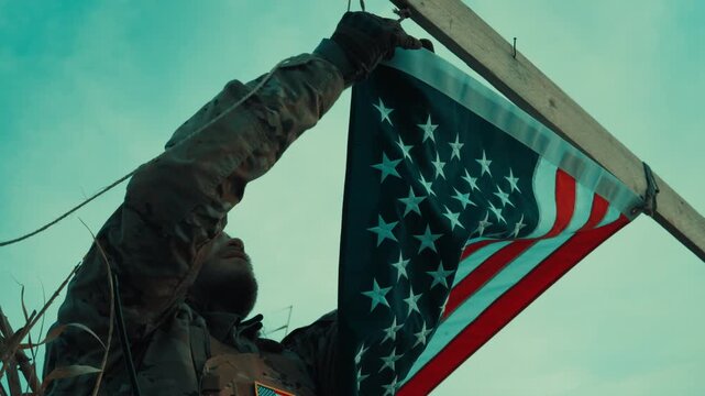 A soldier sets up an American flag at a makeshift base in desert Memorial day