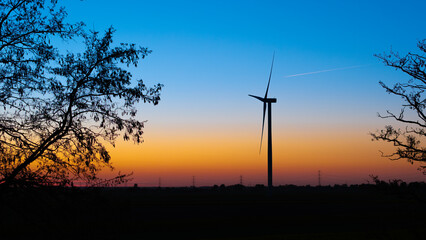 Obraz premium Silhouette Wind Turbine against Colorful Sunset Sky with Tree Branches