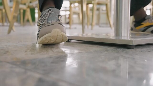 Cafe undertable sneaker closeup captures black man barista playfully nudging partner shoe under table during casual date, tiled floor reflections, espresso cups, candid flirtation and chemistry