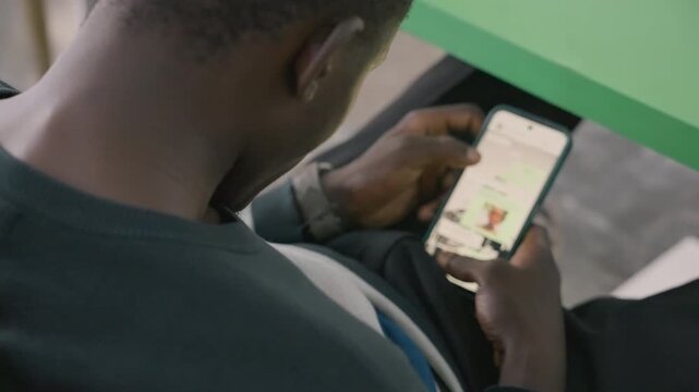 Black man scrolling dating app on phone, sitting at green table, checking messages and profiles, fingers tapping screen, app icons visible, casual sweater, candid focused moment, planning meetup
