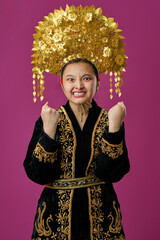 Naklejka premium Young Indonesian Asian Girl in Traditional Gold Headdress and Embroidered Robe Celebrating With Excited Expression