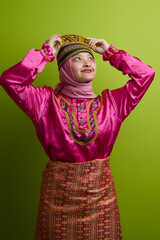 Naklejka premium Young Indonesian Asian Woman Wearing Traditional Malay Costume With Embroidered Hat And Pink Hijab On Green Background