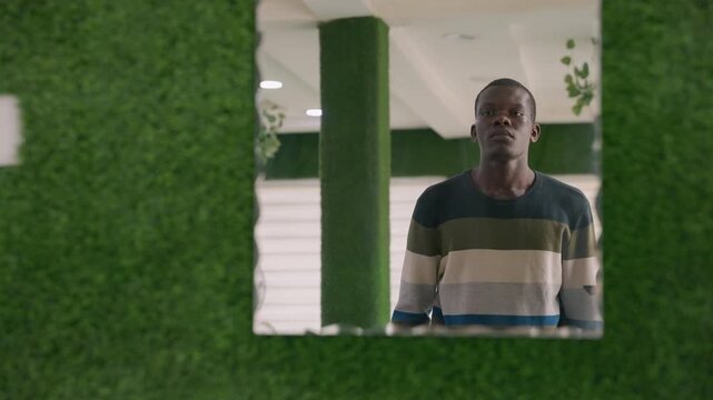 Black man looking down after date in indoor green lobby, striped sweater, hands near face, somber expression, reflective mood, awaiting message, cinematic low light, subtle loneliness