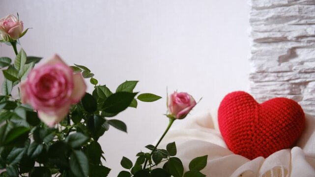 Cozy interior still life composition featuring a knitted heart, a soft warm scarf, and a fresh blooming rose. The warm color palette and soft lighting create a welcoming, homely atmosphere. Comfort, h
