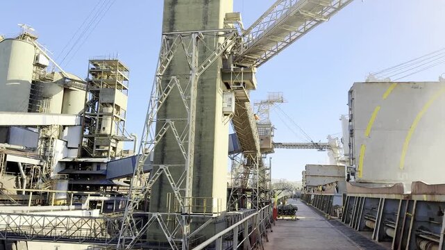 bulk carrier ship berthed at port. loading wheat cargo from special grain terminal. clouds of dust from grain. conveyors silo belt pipes.