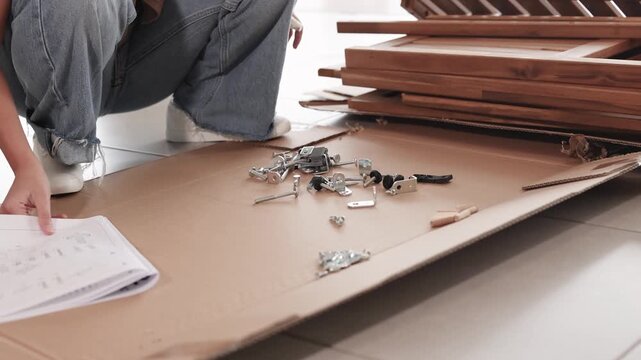Woman sitting on floor and reading furniture assembly manual and checking hardware components.
