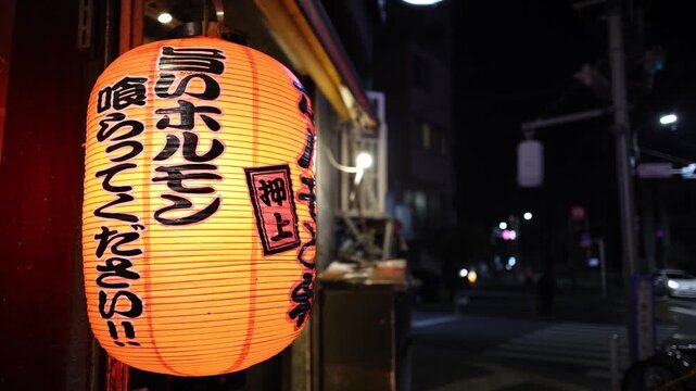 Traditional Japanese red lantern hanging outside local restaurant at night with soft city bokeh background in Tokyo.