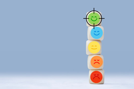 Stacked wooden cubes with different emotion icons from negative to positive and target mark on happy face. Concept of customer satisfaction, feedback analysis, audience targeting and service quality.