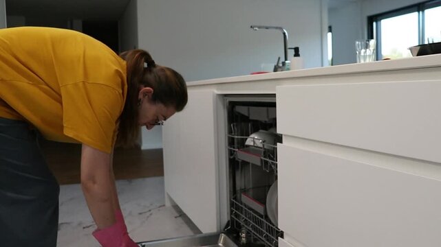 Young woman placing detergent tablet into dishwasher dispenser in modern kitchen. Household routine for appliance use, dish washing preparation, cleaning cycle and home maintenance