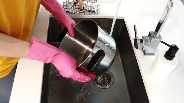 Woman washing cooking pot by hand in kitchen sink with gloves. Home cleaning routine for dish washing, household chores, hygiene, cookware care and domestic lifestyle. Cleaning, big sink