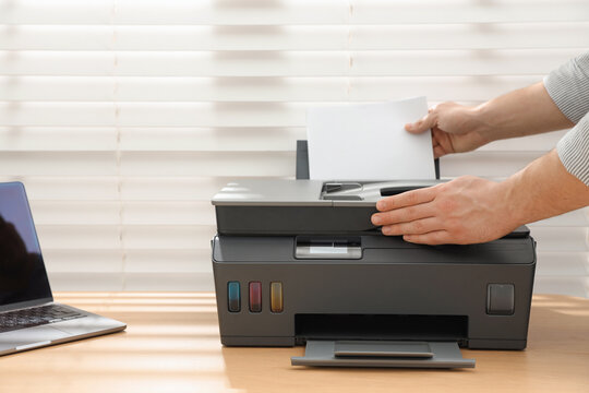 Man loading paper into printer at wooden desk indoors, closeup
