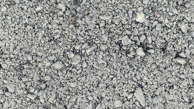 A high-angle, close-up shot of fresh grey asphalt, showing a dense, textured mixture of small crushed stones, angular mineral aggregates, and fine bitumen binder particles.