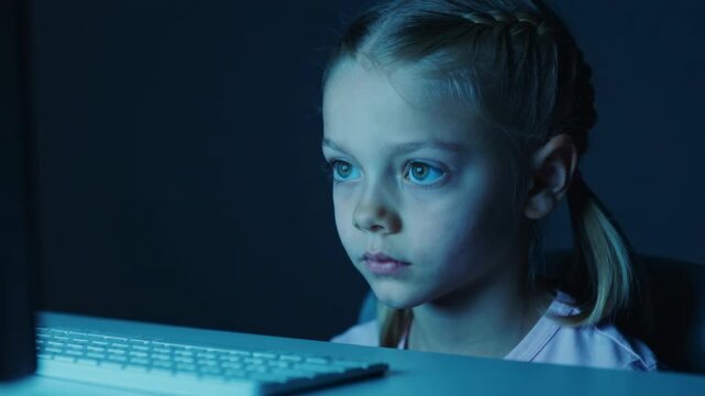 Young girl looking at computer screen in dark room close up