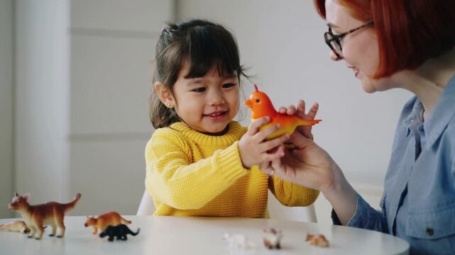 Young girl and woman playing with orange bird toy on white table, medium shot
