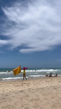 Lifeguard walking on beach with yellow flag and red rescue board