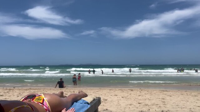 Woman sunbathing on beach with ocean waves and people in background