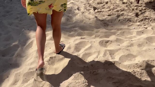 Young woman in yellow dress walking on sandy beach during summer vacation