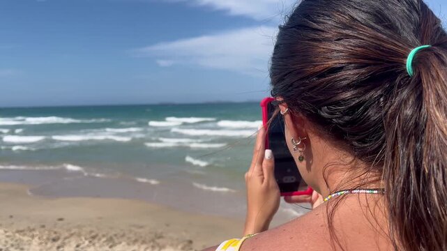Young woman filming beach landscape with smartphone on summer vacation