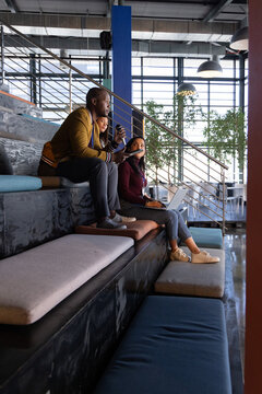 Diverse coworkers collaborating on tiered seating in coworking with laptop and phone by staircase