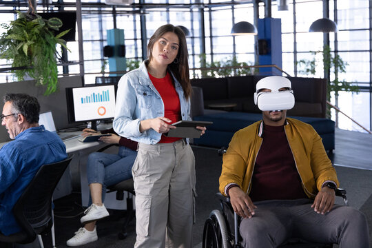 Coworkers holding tablet and stylus, using VR headset in wheelchair at office monitors charts