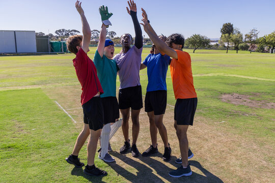 Male teammates celebrating, standing on mown cricket pitch showing crease markings and batting pad