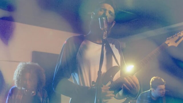Cam moving closer, lead singer strumming, singing into retro mic for music set, lens flares pulsing