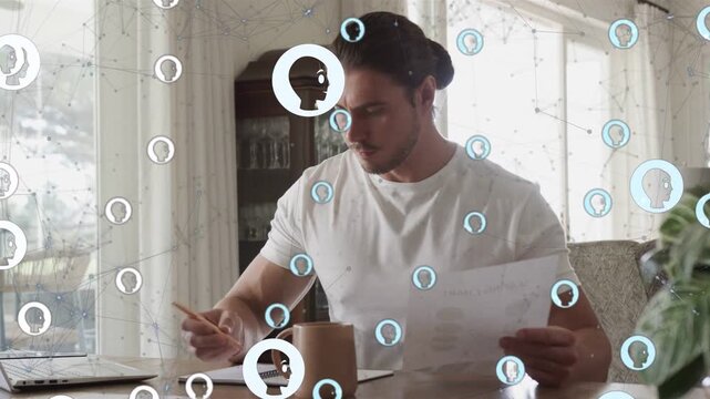 Man with bun reading paper, reaching laptop and writing notes for business, network nodes obscuring