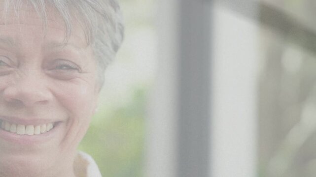 Senior woman facing glass, tilting, causing ghost overlaying face, revealing broad smile for health