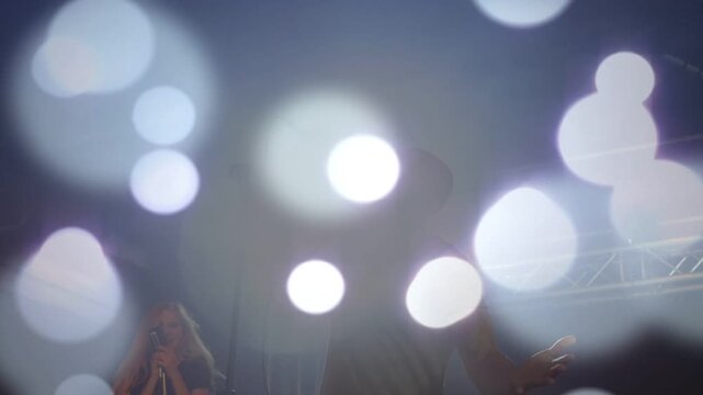 Music lead singer leaning, singing into mic, backup singers moving, bokeh overlay obscuring singers