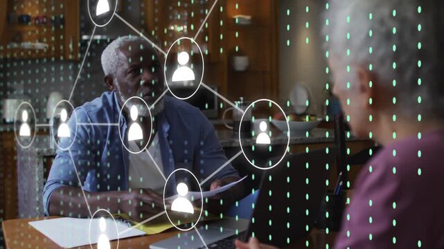 Man reviewing papers, woman at laptop entering data, initiating finance user icon overlaying them