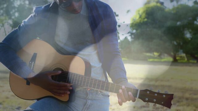 Male musician tuning then fingering and strumming acoustic guitar for music clip, sun flares