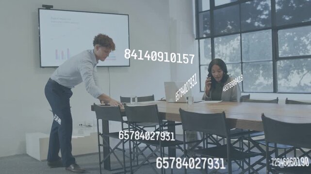 Man glancing at display sorting papers, woman taking call, data overlay showing graphs for business