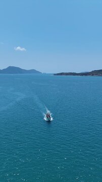 Sailboat Glides Peacefully on Vast Blue Sea with Distant Island and Hills Under Clear Sky, Evoking Tranquility on Ocean Horizon	