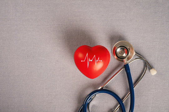 Red heart with an ECG pulse line and blue stethoscope on gray fabric background. for healthcare, cardiology, medical checkup, and heart disease awareness concepts.