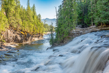 Water cascades over rocks in a serene forested landscape during a clear day © Lost_in_the_Midwest