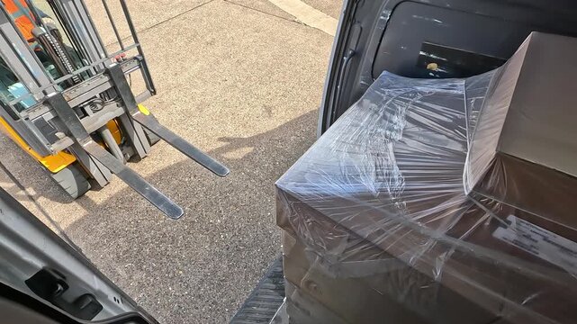 Forklift approaching a delivery van and starting to unload pallet cargo. Warehouse logistics, transportation and supply chain operations concept.