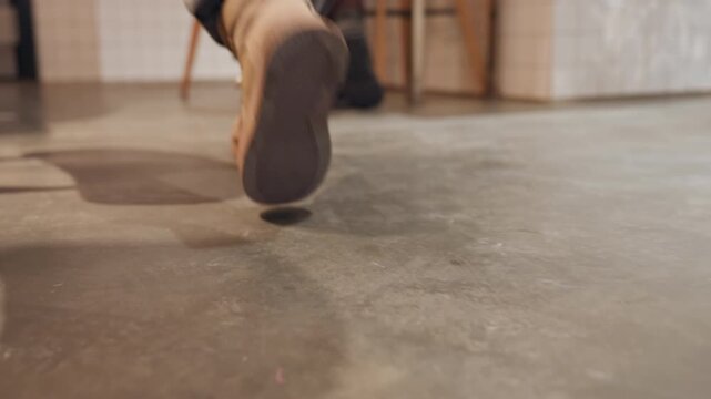 Cafe floor closeup boots under table. Solitary customer tapping foot in tan boots, denim cuffs brushing concrete floor beside wooden chair legs warm light and soft shadow, subtle scuff marks, slow