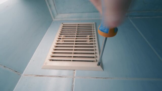 Dirty Ventilation Grille Unscrewing with Screwdriver on Blue Tile Floor | HVAC Vent Cover Removal for Cleaning and Maintenance | Home Air Duct Service Close-Up Wide-Angle