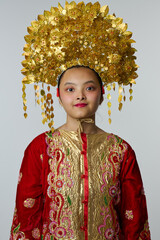Naklejka premium Young Indonesian Asian Girl Wearing Ornate Gold Headdress and Embroidered Red Traditional Costume Portrait