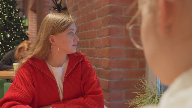 Observant woman seated. Woman listens in cozy cafe. Profile of woman with joyful expression. Casual urban setting in focus. Intimate cafe scene showing woman engaged in quiet reflection