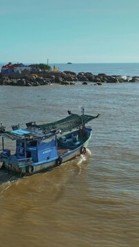 A lone fishing boat sails on the calm waters near Hon da Chu, Nha Trang, Vietnam. The sun glints off the sea as the boat heads towards the shore