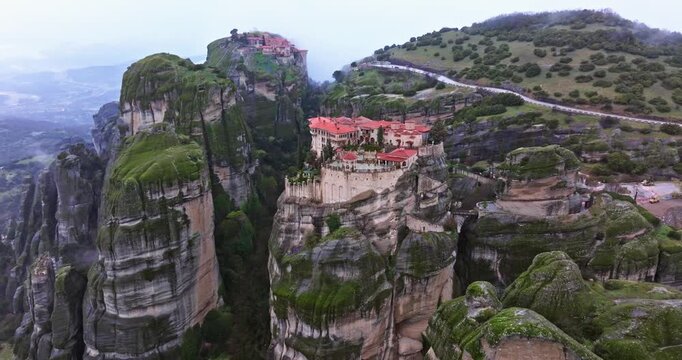 Breathtaking aerial drone footage of Meteora in Kalambaka, Greece, captured in a mystical foggy atmosphere. The iconic monasteries perched atop towering rock formations emerge through the mist, while 
