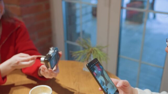 Cozy cafe table friends comparing camera, closeup of hands exchanging vintage camera and smartphone, cups of coffee on wooden tabletop, window light and warm brick interior, casual discussion