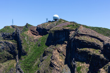 Fototapeta premium Mountain peak with radar station on Pico do Areeiro. Rugged volcanic terrain surrounds PR1 Vereda do Areeiro hiking trail. Clear skies highlight Madeira's scenic high-altitude landscape.