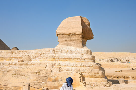 A female tourist admires the ancient Sphinx with the Great Pyramid of Giza and the smaller Pyramid of Queen Meritetis behind, in Giza, Egypt.