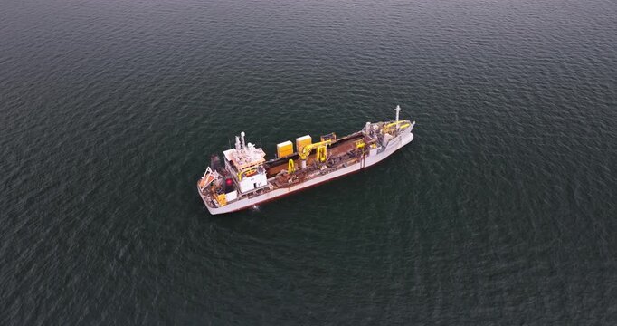High-quality aerial footage of a dredger support vessel, also known as a subsea cable ship, operating in a busy industrial port. The vessel is designed for underwater cable installation, maintenance, 