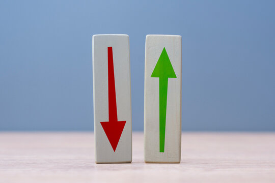 Two wooden blocks with red down arrow and green up arrow standing on a table. Concept financial growth and decline, profit and loss, stock market trends, forex trading and business performance.