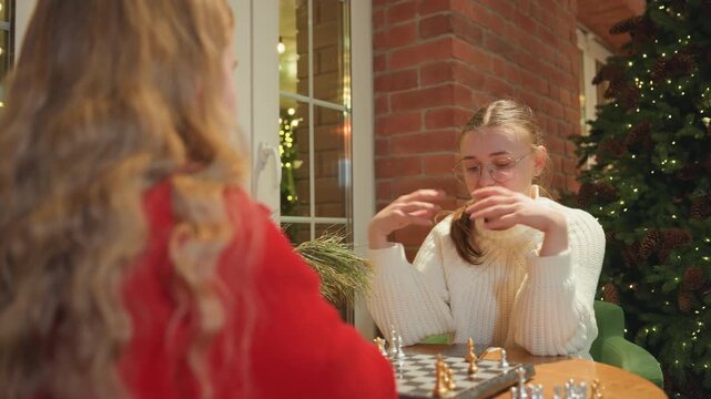 Player celebrates quiet victory at cafe, smiling opponent watches across chessboard, checkmate move revealed among mugs and scattered pieces, holiday lights and evergreen backdrop, soft laughter