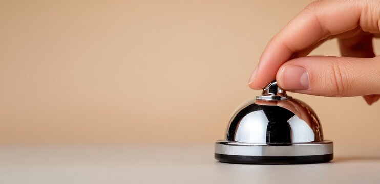 hand pressing a shiny chrome service bell on a countertop with a neutral beige background, conveying polite request and anticipation