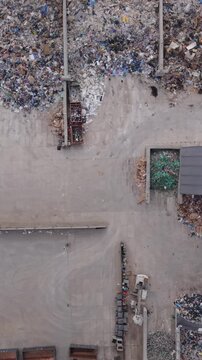 Vertical screen Aerial View Landfill Warsaw Showing Scattered Waste Piles, Compactor Vehicles, Open Containers And Sorting Lines, Overcast Industrial Mood, Slow Drone Sweep Revealing
